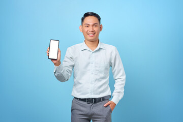 Smiling young handsome businessman showing smartphone blank screen in hand on blue background