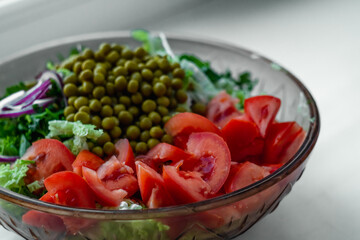 Fresh vegetable salad with tomatoes and green peas in a glass bowl on a white background.