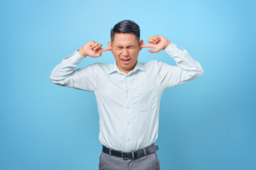 Naklejka premium Frustrated young handsome businessman covering ear with anger expression on blue background
