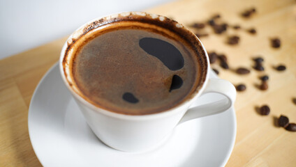 a cup of black coffee for morning caffeine. a shot of a hot coffee on the wooden table with some coffee beans around.