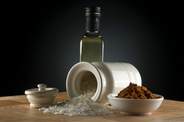 Fototapeta na wymiar Olive oil bottle with paprika in bowl and rice spilling out of white canister on timber bench