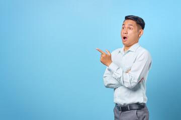 Shocked young handsome businessman pointing finger away at copy space on blue background