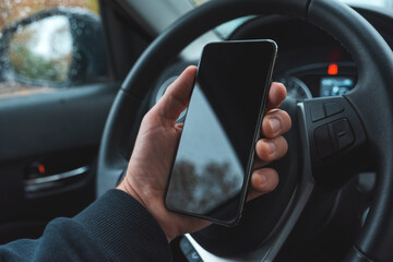Car driver holding mobile smart phone over steering wheel, blank black screen