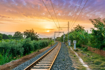 Plakat old evening railroad leading to a sunset glow in mountains with green bushes and cjlorful cloudy sku on the background