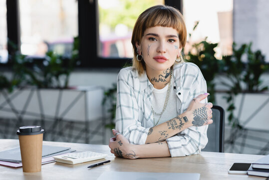 young tattooed businesswoman sitting with crossed arms at workplace in office