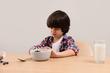 Cute little boy refusing to eat his breakfast at table on grey background