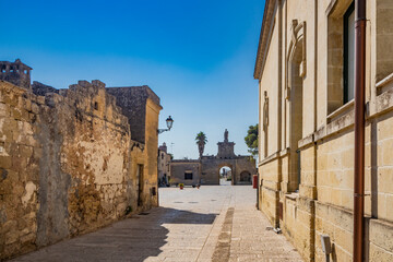 The small fortified village of Acaya, Lecce, Salento, Puglia, Italy. The stone-paved square. An alley of the village leads to the large entrance door, with the large arch and the stone statue.