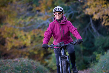 ympathetic active senior woman, riding her electric mountainbike in the colorful autumn forests of the Bavarian Alps near Oberstaufen, Germany