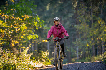 ympathetic active senior woman, riding her electric mountainbike in the colorful autumn forests of...