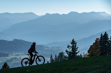 Woman as silhouette riding her electric mountain bike in the Allgaeu alps near Oberstaufen with awesome view into the Bregenz Wald Mountains, Vorarlberg , Austria, people
