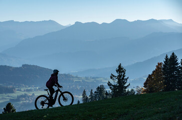 Fototapeta premium Woman as silhouette riding her electric mountain bike in the Allgaeu alps near Oberstaufen with awesome view into the Bregenz Wald Mountains, Vorarlberg , Austria, people 