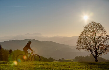 active woman riding her electric mountain bike at sunset in front of the awesome silhouette of...