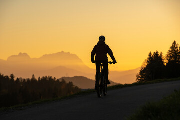 active woman riding her electric mountain bike at sunset in front of the awesome silhouette of Mount Saentis, Appenzell switzerland