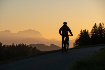 active woman riding her electric mountain bike at sunset in front of the awesome silhouette of Mount Saentis, Appenzell switzerland