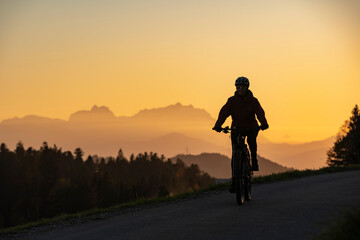 active woman riding her electric mountain bike at sunset in front of the awesome silhouette of Mount Saentis, Appenzell switzerland