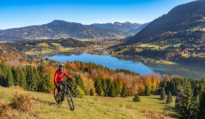 nice  woman with electric mountain bike enjoying the view over lake  Alpsee in atumnal atmosphere  in the Allgaeu alps above  Immenstadt, Bavarian Alps, 