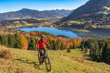Fototapeta na wymiar nice woman with electric mountain bike enjoying the view over lake Alpsee in atumnal atmosphere in the Allgaeu alps above Immenstadt, Bavarian Alps, 
