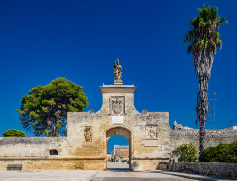 The small fortified village of Acaya, Lecce, Salento, Puglia, Italy. The large stone-paved square. The gateway to the city, with the large arch and the stone statue.