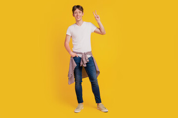 Fototapeta na wymiar Full length photo of young cheerful guy standing hand in pocket show peace cool v-sign isolated over yellow color background