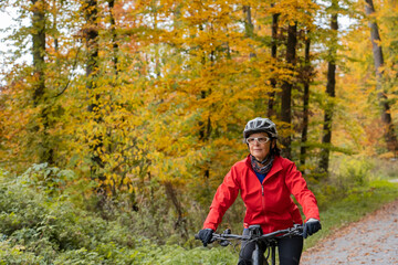 Obraz premium pretty senior woman ridin her electric bicycle in a colorful autumn forest with golden foliage 