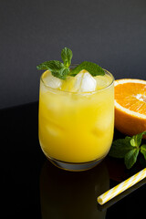 Close-up on orange juice with ice in the drinking glass on the black background. Copy space. Location vertical.
