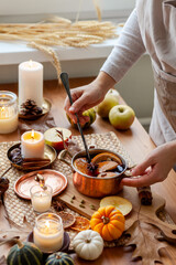 Young woman preparing hot autumn drink: mulled wine with spices, fruits. Natural ingreduents: cinnamon, anise, cardamon, clove, apple, orange. Cozy home atmosphere