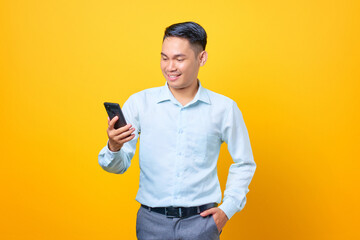 Smiling young handsome businessman looking at mobile phone screen on yellow background