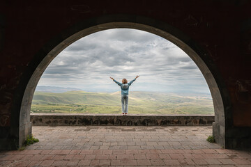Happy woman with outstretched arms admires the view of the landscape near the Charents Arch in...
