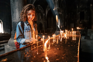 A woman puts a candle and prays in a church or Catholic church. The concept of sorrow and hope in...