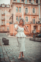 Close up fashionable woman portrait of young pretty fashionable girl posing in city in Europe, summer street fashion, holding retro hat. Fashion chic
