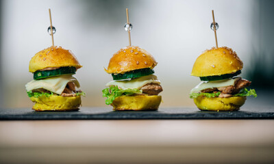 
Close up of three delicious homemade mini chicken cheese  hamburgers on black slate board - obrazy, fototapety, plakaty