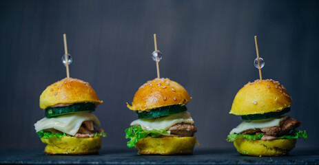 
Close up of three delicious homemade mini chicken cheese  hamburgers on black slate board
