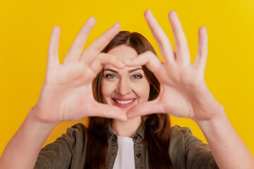 Portrait of dreamy romantic lady show heart fingers cover face on yellow background