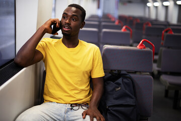 Young man travel by train. Handsome african man talking to the phone..