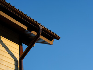 A roof with a gutter on a house against a blue sky background.
