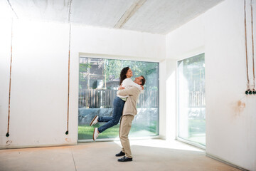 cheerful man lifting pleased african american wife in new house