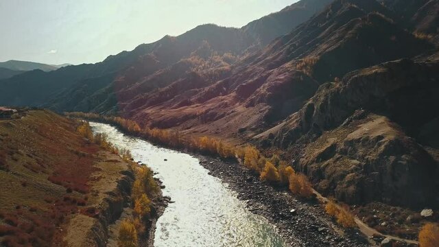 Aerial view of the calm mountain river Katun. Autumn landscape of the wild nature of the Altai Territory: Mountains, forests, fields, a country walking road, the rays of the sun. The camera flies