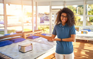 An African American woman sales assistant demonstrates products in a bed, mattress and pillow store.