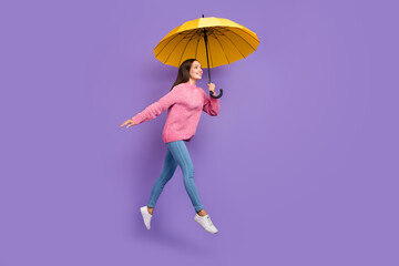 Full length photo of funny young lady run with umbrella wear pullover jeans footwear isolated on purple background