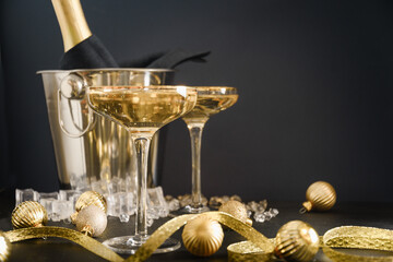 Festive New Year champagne in wineglasses and bottle in bucket decorated Christmas gold baubles on...