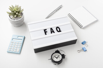 FAQ word on lightbox with office supplies on white desk