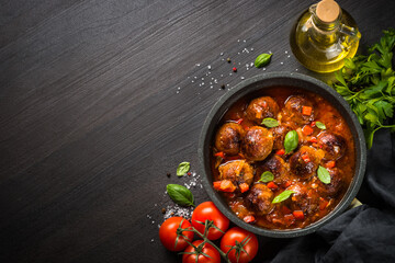 Meatballs in tomato sauce in black skillet on dark stone table. Top view copy space.