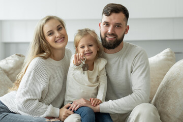 Little girl holds the keys to a new family home in her hands. Portrait of a smiling young married couple and a cute girl showing the keys