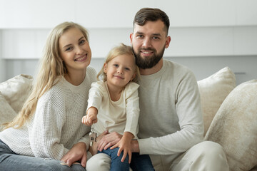 Little girl holds the keys to a new family home in her hands. Portrait of a smiling young married couple and a cute girl showing the keys