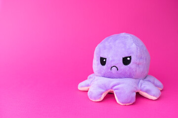 Isolated photography of violet plush octopus toy. Toy is used to express emotions. Octopus has angry face. Purple background.