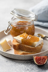 Fototapeta na wymiar Breakfast toasts with brie cheese and fig jam on ceramic plate. Healthy gourmet snack. vertical image