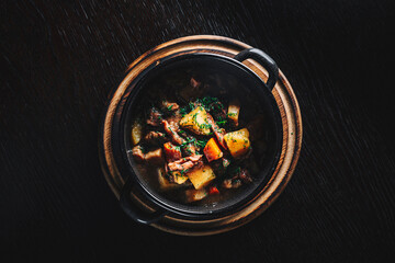 Goulash. Vegetable rague with meat, eggplant, pepper, potato and carrot in black bowl on dark wooden background