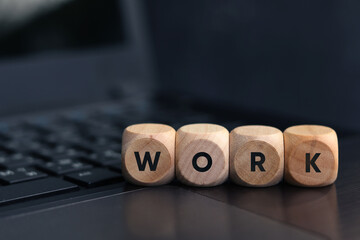 Wooden cube with the word WORK on laptop keyboard background