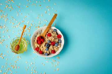 Organic oat flakes with blueberries and raspberries and honey over colorful background. Macro photo of natural raw food ingredient for healthy vegan and vegetarian diet. Flat lay