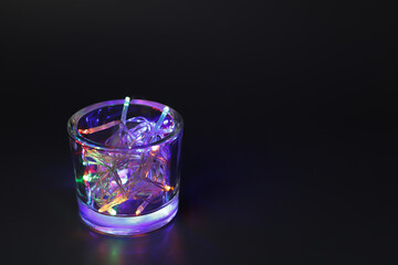 Glass with Christmas lights on black background.